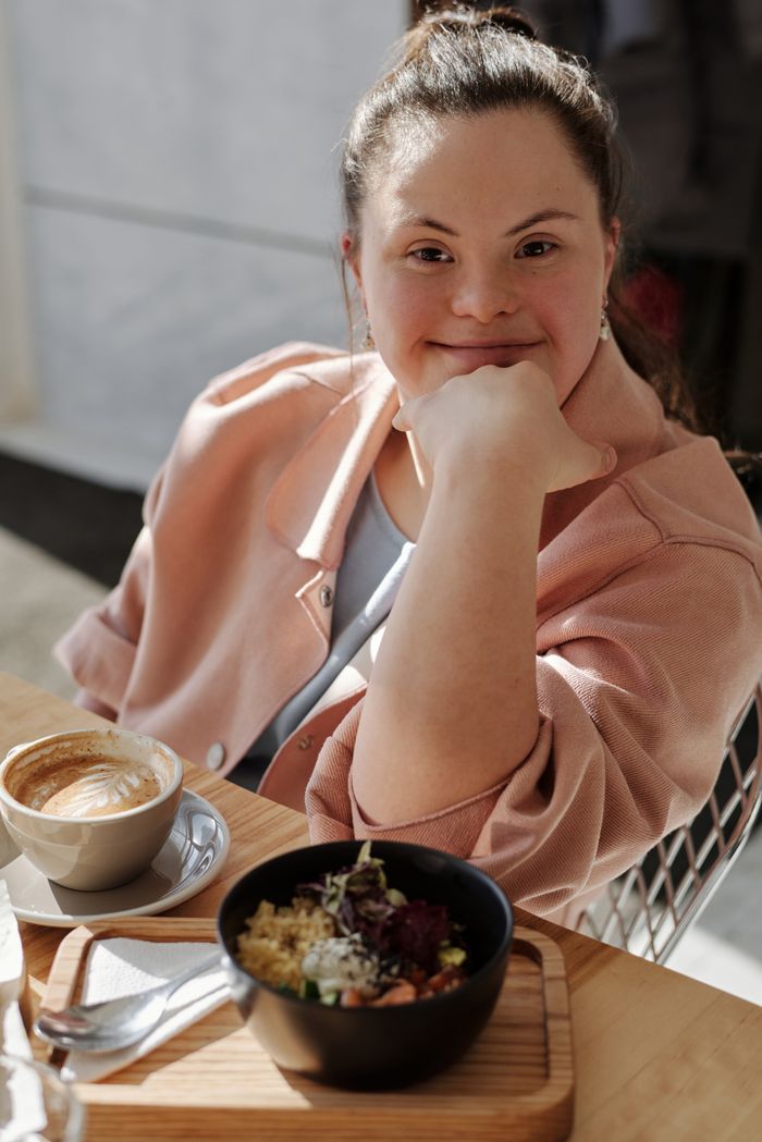 Smiling young woman with down syndrome enjoying breakfast and coffee at a café.