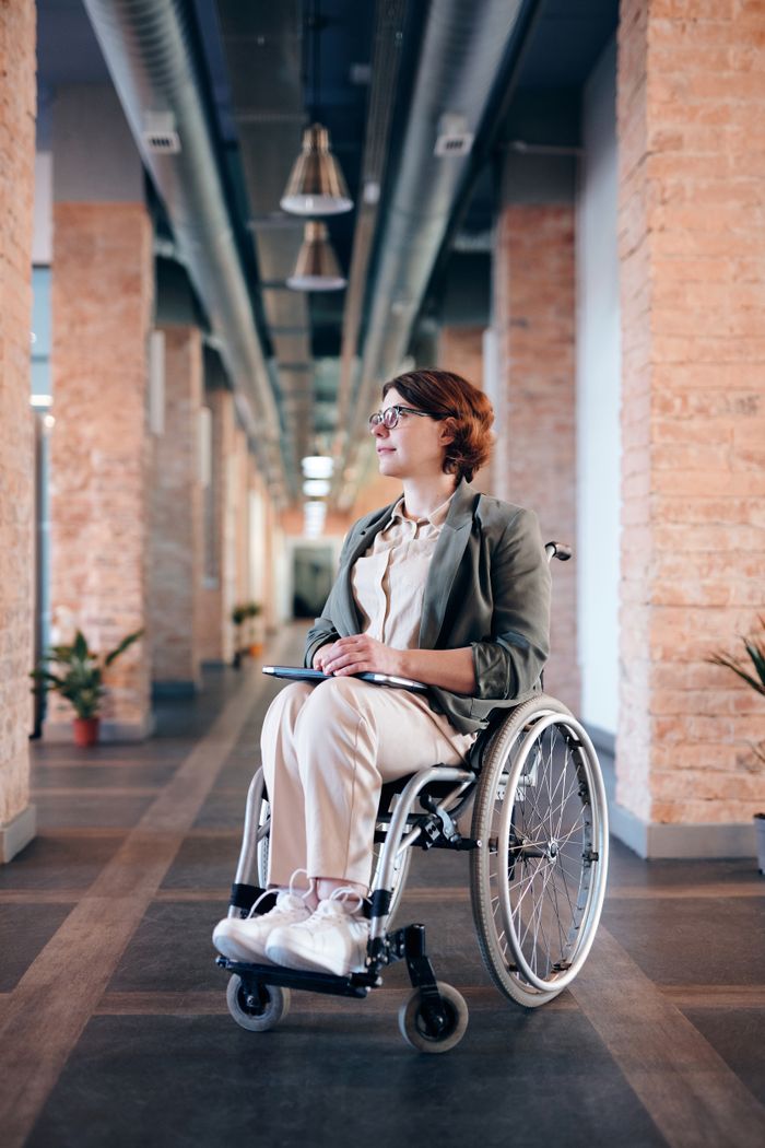 Confident businesswoman in wheelchair in a modern office corridor, contemplating and working.