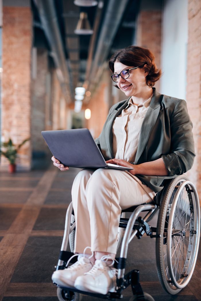 Smiling businesswoman in a wheelchair working on a laptop in modern office.