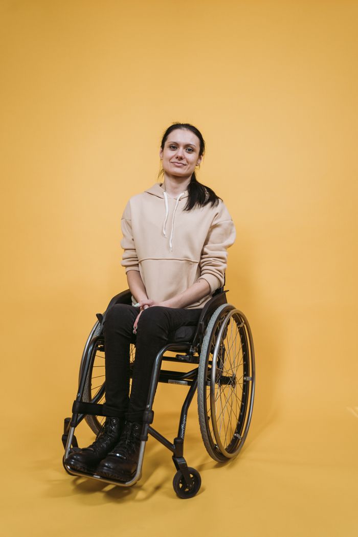 services-01 Portrait of a woman sitting in a wheelchair against a bright yellow background.