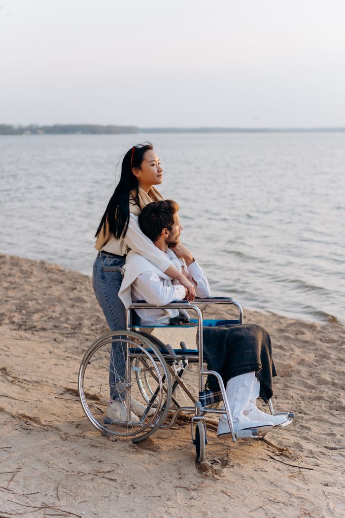 services-03 A loving couple enjoys a serene beach scene, with one partner in a wheelchair.