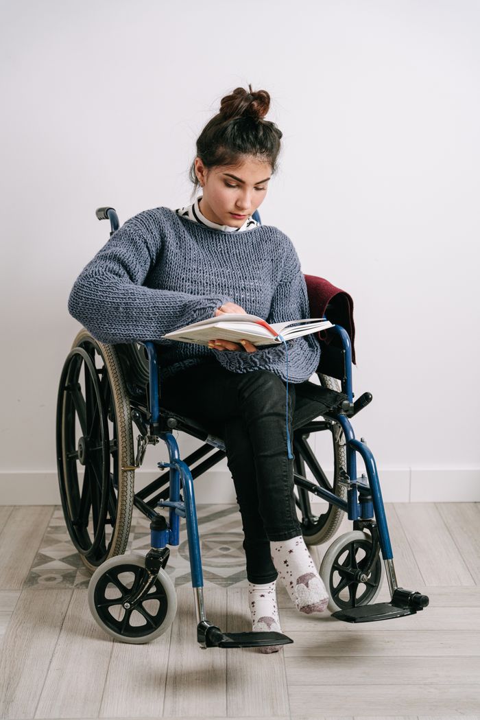 services-02 A young woman in a wheelchair reading a book indoors, showcasing empowerment and learning.
