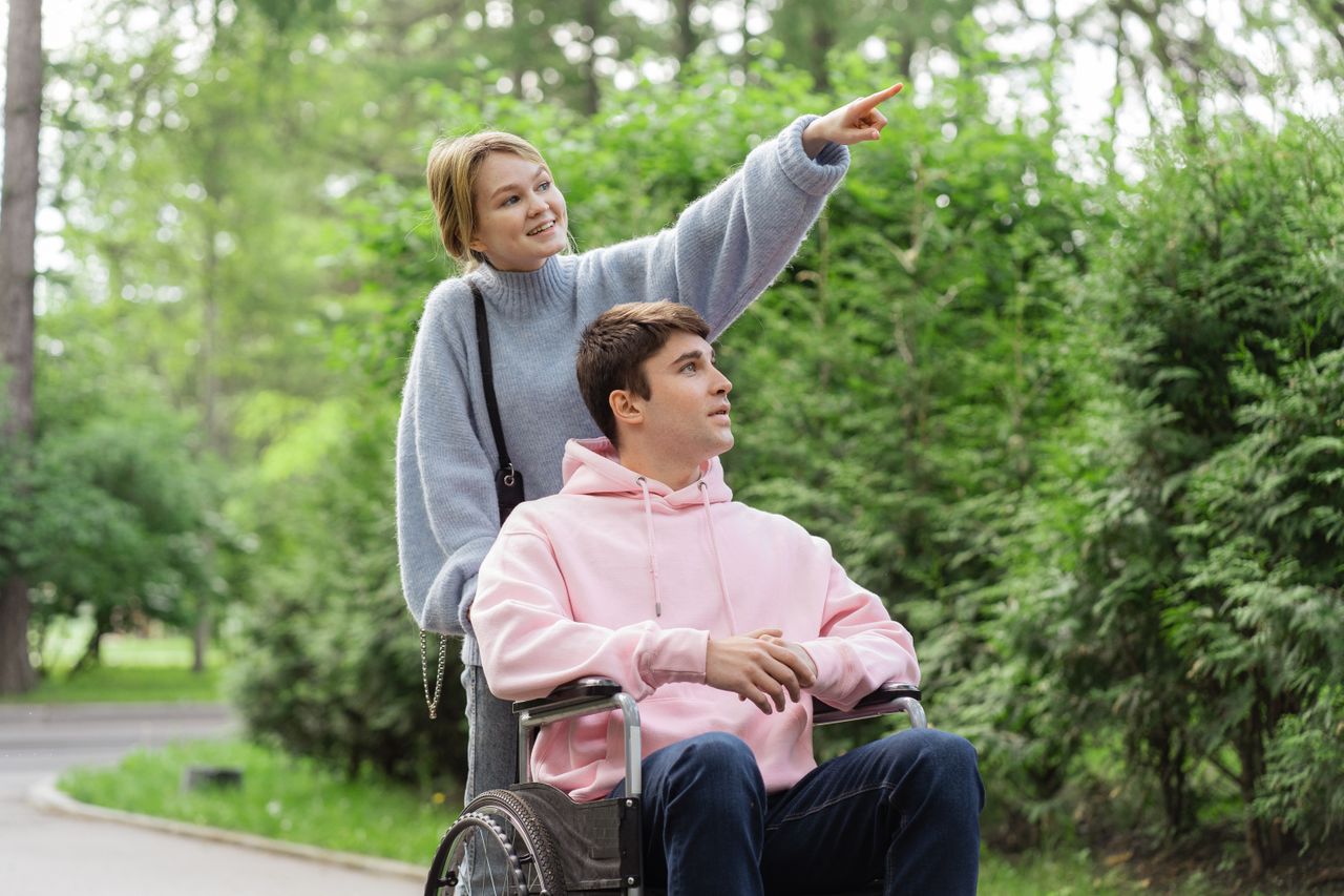 services-img A happy couple enjoying nature, with a wheelchair, pointing towards the trees.