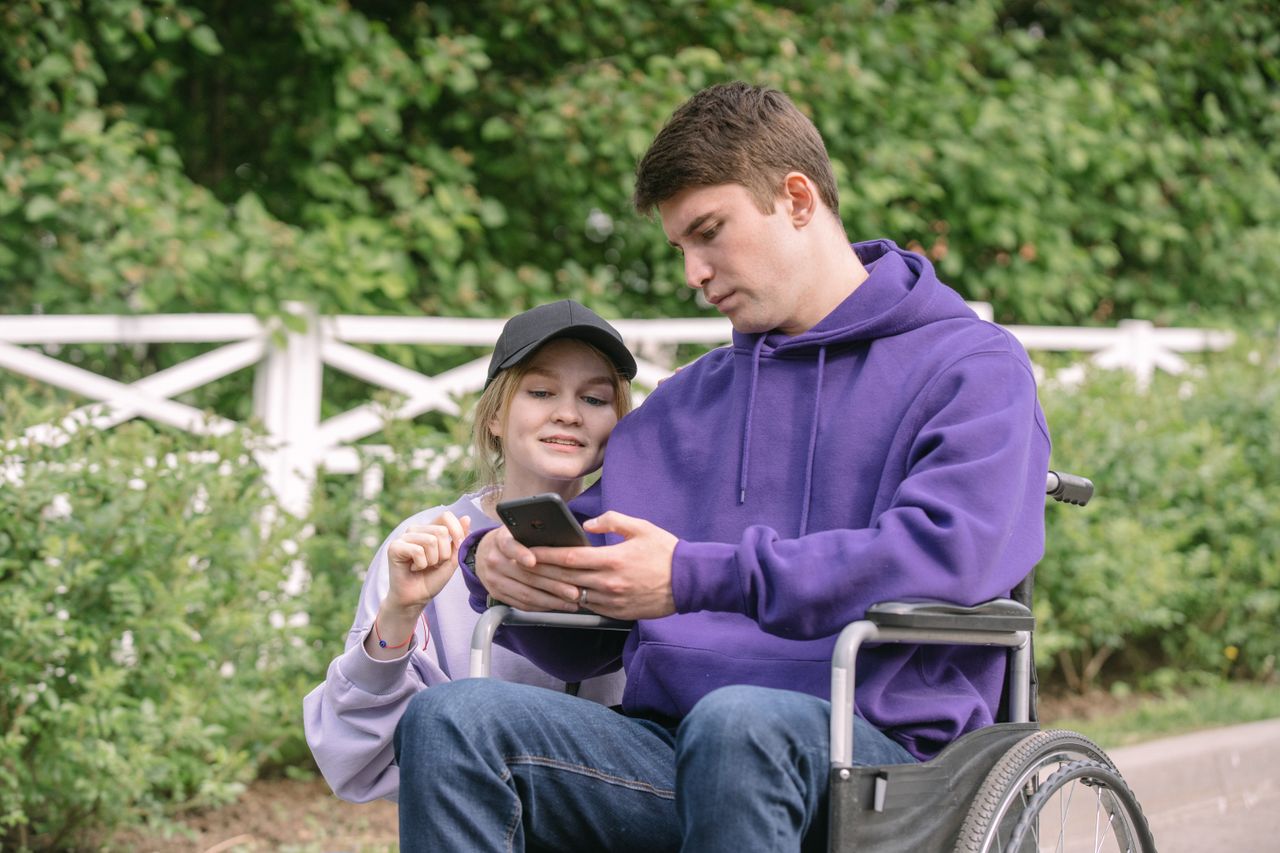 A young couple sitting together, using a smartphone on a sunny day in the park.