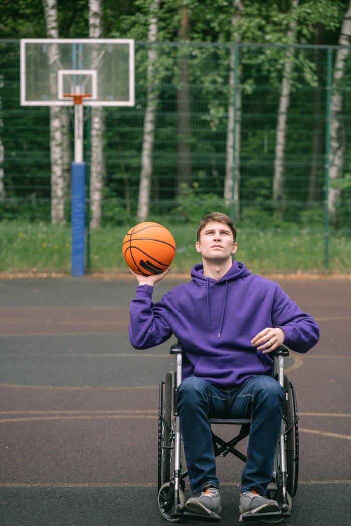 about-img Young man in wheelchair playing basketball on an outdoor court, displaying determination and skill.